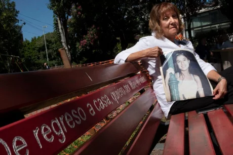 La mamá de la adolescente, en el banco rojo que se puso en el lugar del crimen.. Imagen: Télam